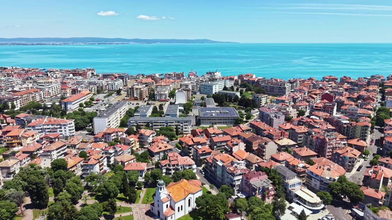 Panorama cittadino con tetti rossi, parchi verdi e mare blu sotto un cielo limpido in una giornata di sole in una località costiera.
