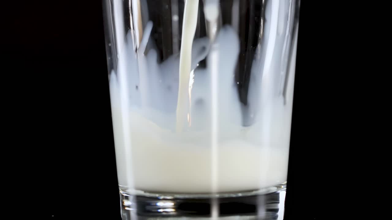 A close-up view of milk being poured into a glass against a dark backdrop.