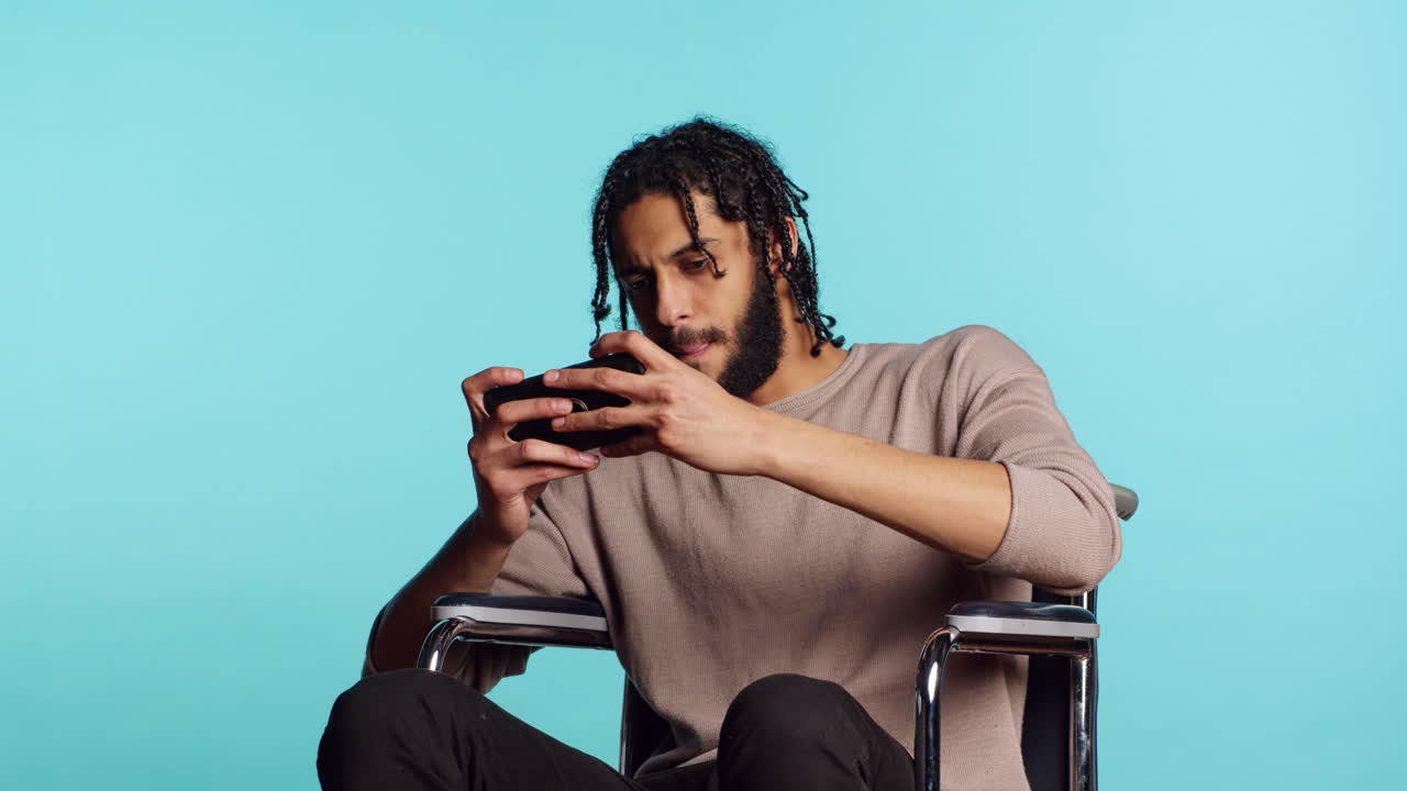 Man in wheelchair playing videogames on cellphone, celebrating victory, studio