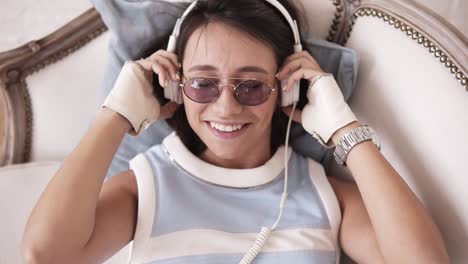 attractive cheerful girl with headphones and glasses smiling and dancing to the music while lying on the sofa