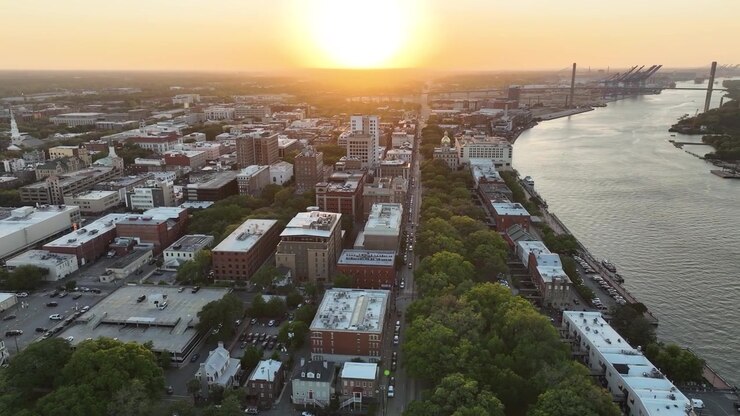 Ripresa con drone al tramonto del quartiere storico di Savannah, con i punti di riferimento a cupola dorata della città, i battelli fluviali e il caldo bagliore del crepuscolo sul fiume Savannah.
