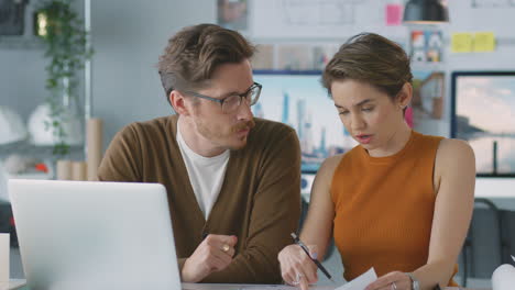 Männliche-Und-Weibliche-Architekten-Im-Büro-Arbeiten-Am-Schreibtisch-Am-Laptop-Und-Betrachten-Pläne