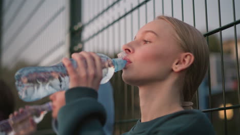 ladies relaxing outdoors after exercise, seated and drinking water from bottles to stay hydrated, enjoying a well-deserved break after an intense workout session