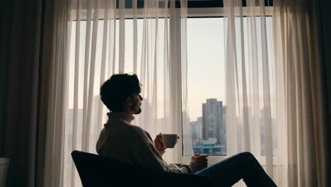 man enjoying a drink by the window with a city view