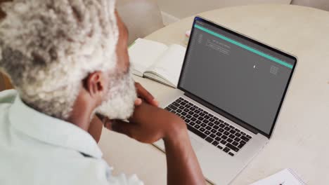 hombre afroamericano sentado en el escritorio viendo el procesamiento de datos de codificación en la pantalla del portátil