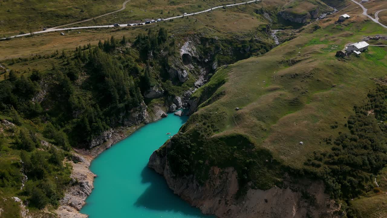 Yeşil tepeler ve kıvrımlı yollarla çevrili, turkuaz sulara sahip Mont Cenis Gölü'nün havadan görünümü.