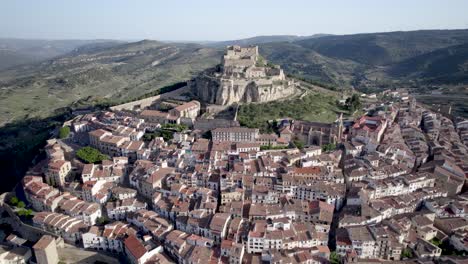 Vista-Frontal-De-Drones-De-4k-Hacia-El-Antiguo-Castillo-Y-Las-Murallas-Defensivas-En-La-Cima-De-Una-Colina-Rocosa-Entre-Los-Tejados-De-Morella-En-Un-Día-Soleado,-Morella,-Maestrazgo,-España