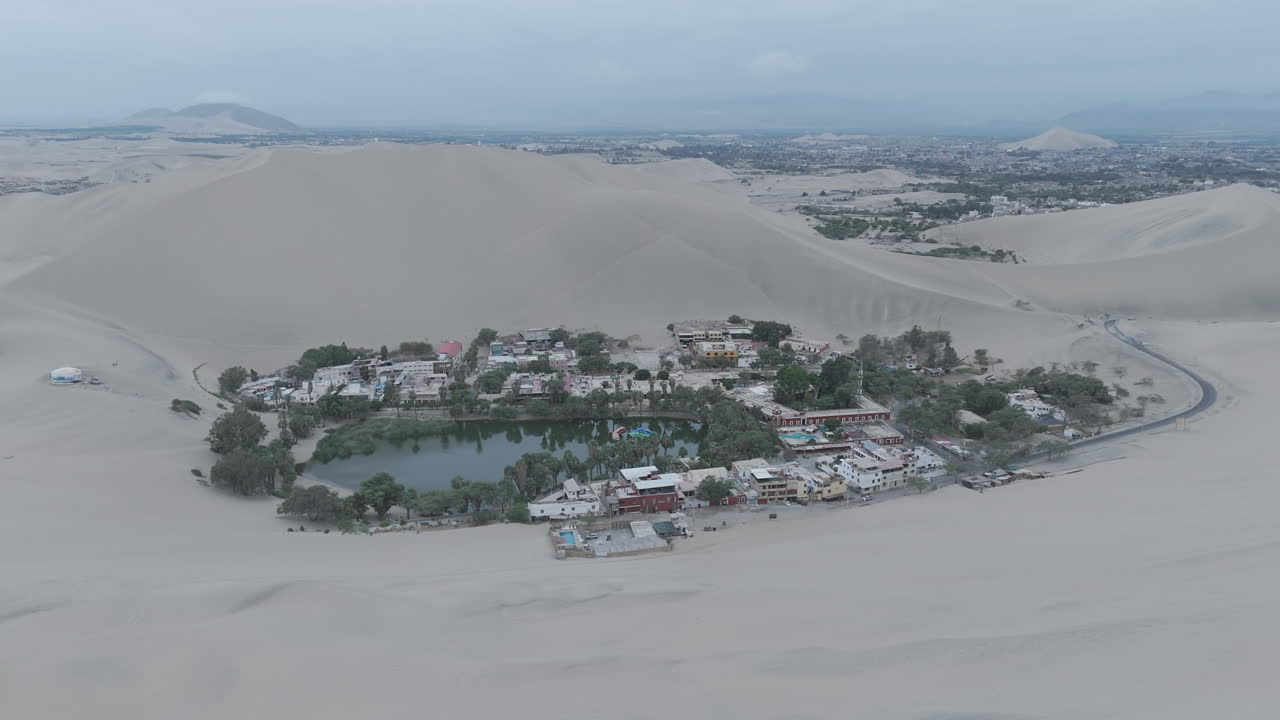 Drone shot revealing the city of Huacachina in Peru behind the dunes on a cloudy day during the mist LOG
