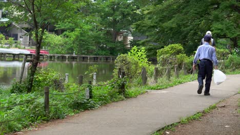 在日本東京的zempukuji公園的夏天,許多人沿著不同的步道散步,在樹木的陰影,湖泊和深綠的自然中清爽自己