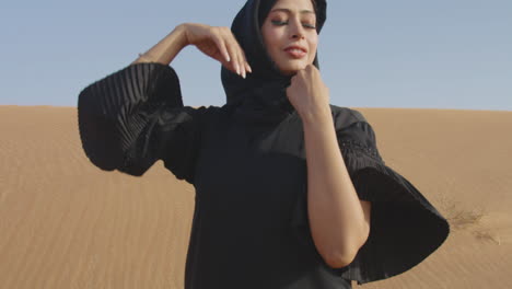 muslim woman wearing traditional black dress and hijab posing in a windy desert 2