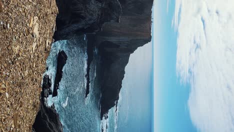 Zambujeira do Mar over the sea shore with ocean waves, cliffs and sand dunes covered by green vegetation red leaves of sour fig, sunny day, clear blue sky