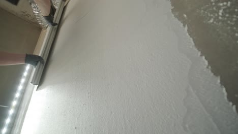 a worker's hand skillfully applies a layer of plaster using a trowel on a wall under bright led lights, showcasing detailed construction work