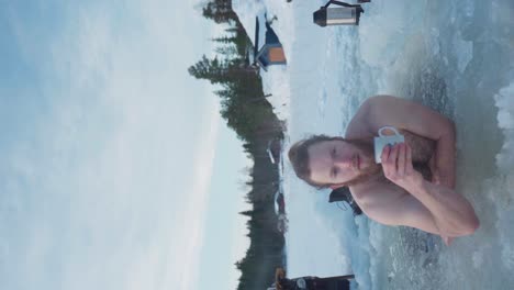 vertical - man drinking cup of tea while submerged in frozen lake water in winter