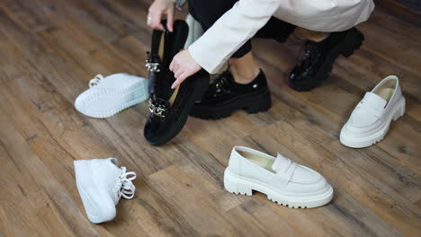 woman in massive black shoes walks among the scattered footwear. lady picks up another pair of black shoes leaving white ones on the floor.