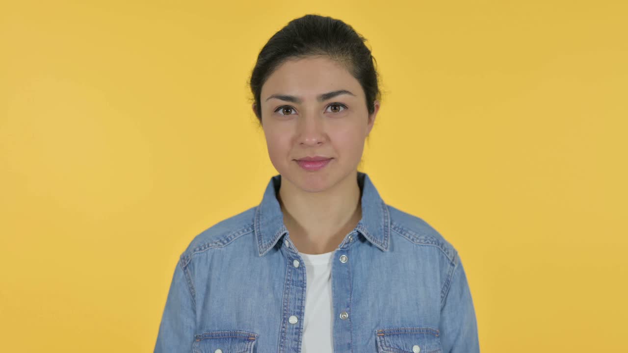 Giovane donna indiana sorridente alla fotocamera, sfondo giallo