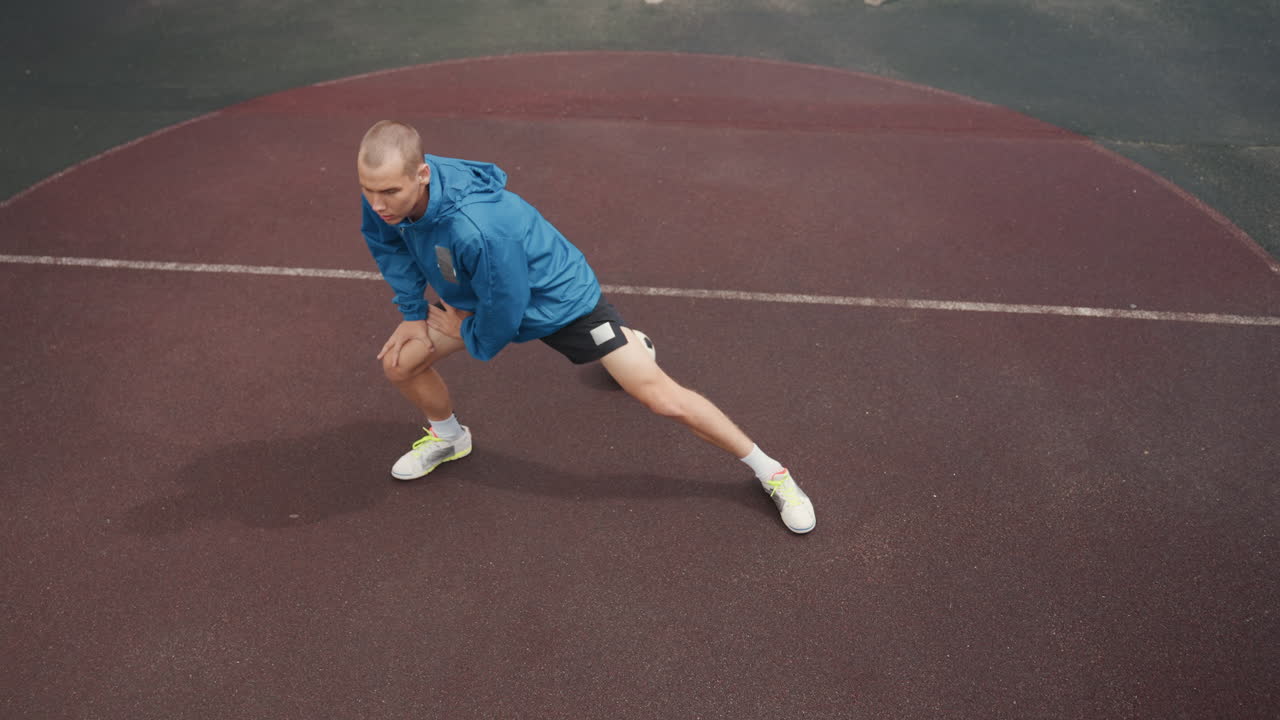 overhead closeup soccer training wet court, male player stretching lateral legs, ball beside foot, raindrops on textured surface, focused expression, dynamic balance and footwork practice