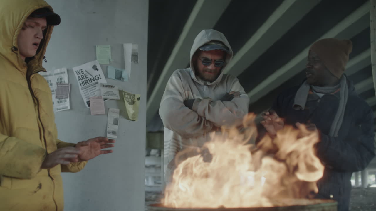 Homeless men huddle around a barrel fire under an overpass