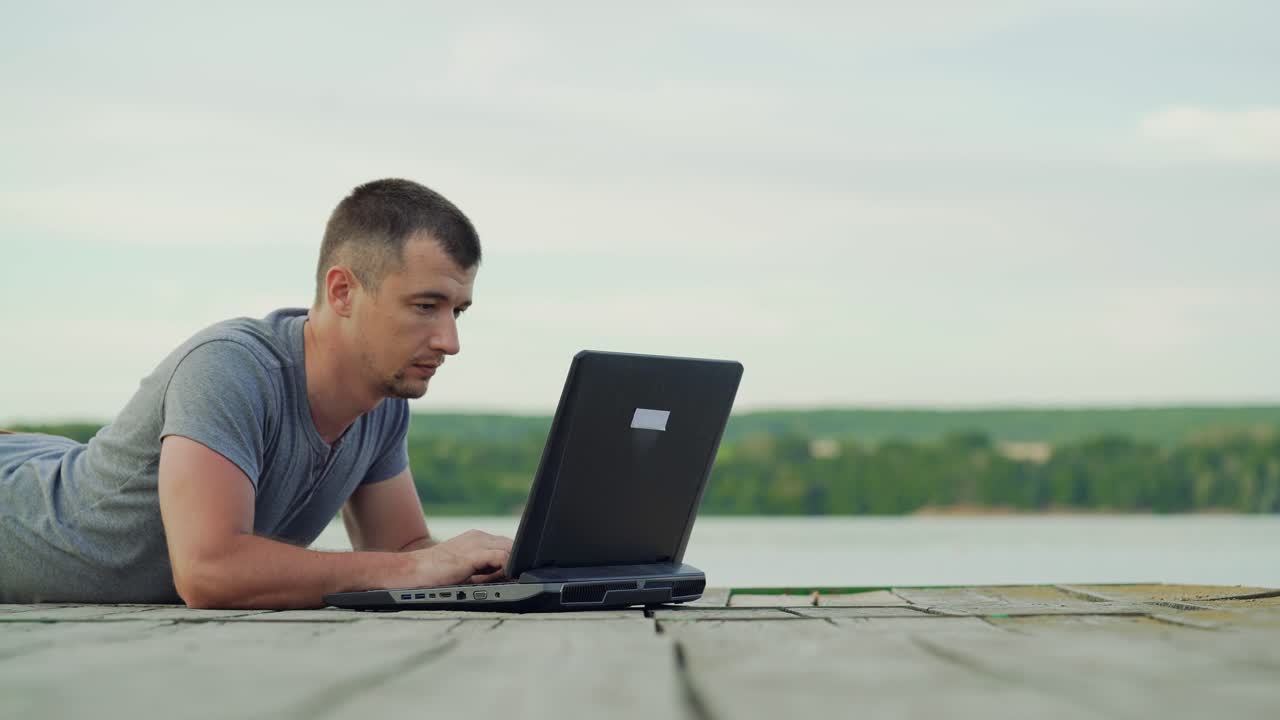 Man working on laptop outdoors. Wooden pier in the lake