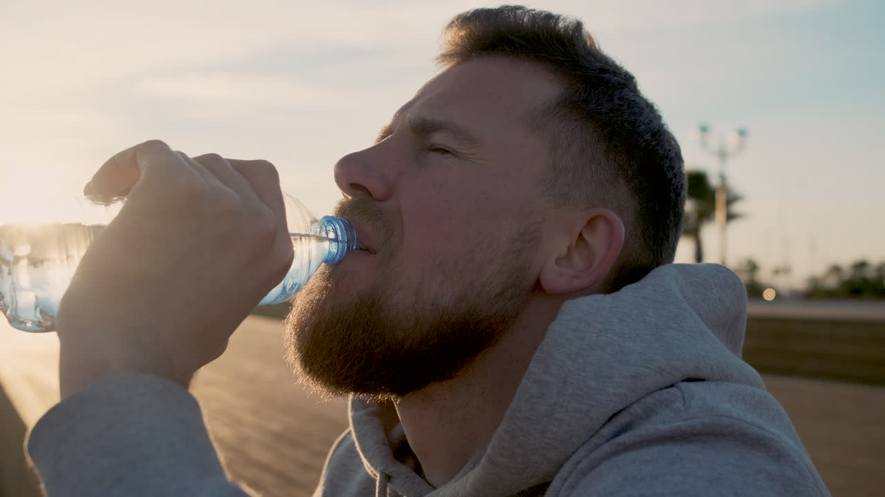 해가 지는 해변에서 물을 마시는 남자