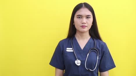 Happy Pretty Asian doctor woman with OKAY sign, ok gesture, correct choice, Isolated on yellow background