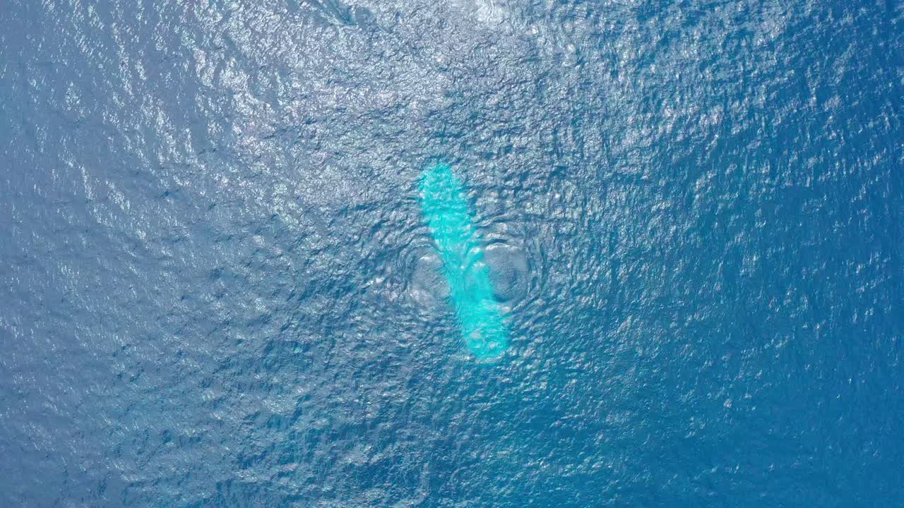 Panning bird's eye aerial shot of a fully submerged submarine descending to the bottom of the ocean floor off the coast of the Big Island of Hawai'i