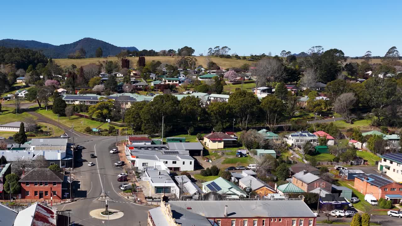 Drone ascends above Dorrigo, revealing rural town, residential streets, shops, and distant hills in daylight