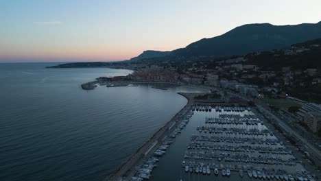 Menton-on-the-french-riviera-at-dusk,-showcasing-the-marina-and-coastline,-aerial-view