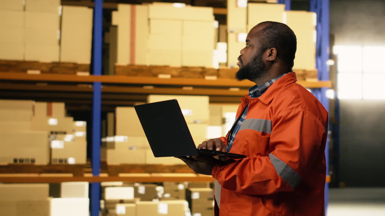 African american employee using laptop to handle logistics in industrial facility