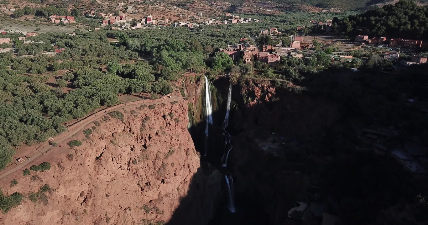 "Morocco's renowned Ouzoud cataracts drop vertically through dramatic gorge formations, where falling torrents generate iridescent mist clouds above serene jade-colored pools."