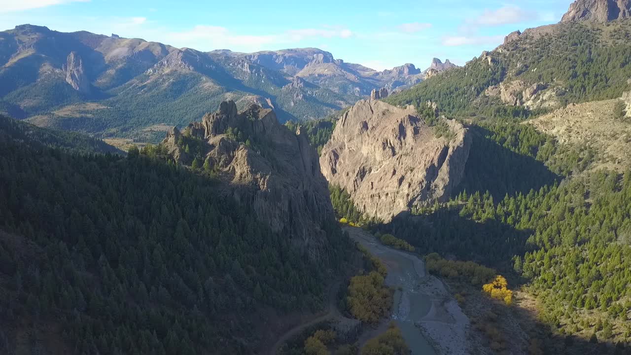 podemos ver un movimiento de cámara sobre una carretera y un río rodeado de grandes montañas rocosas cuando se pone el sol de la tarde