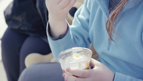 Close-up-of-little-girl-with-blue-jumper-nail-polish-and-teddy-bear-beside-her-holding-a-sundae-ice-cream-sitting-outdoor-4k