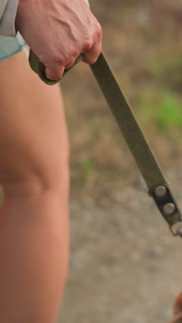 primer plano de una persona con pantalones cortos de vaqueros sosteniendo una correa de perro mientras camina por un camino de tierra, venas de la mano visibles, perro parcialmente visible, entorno rural, fondo borroso con plantas verdes y hierba