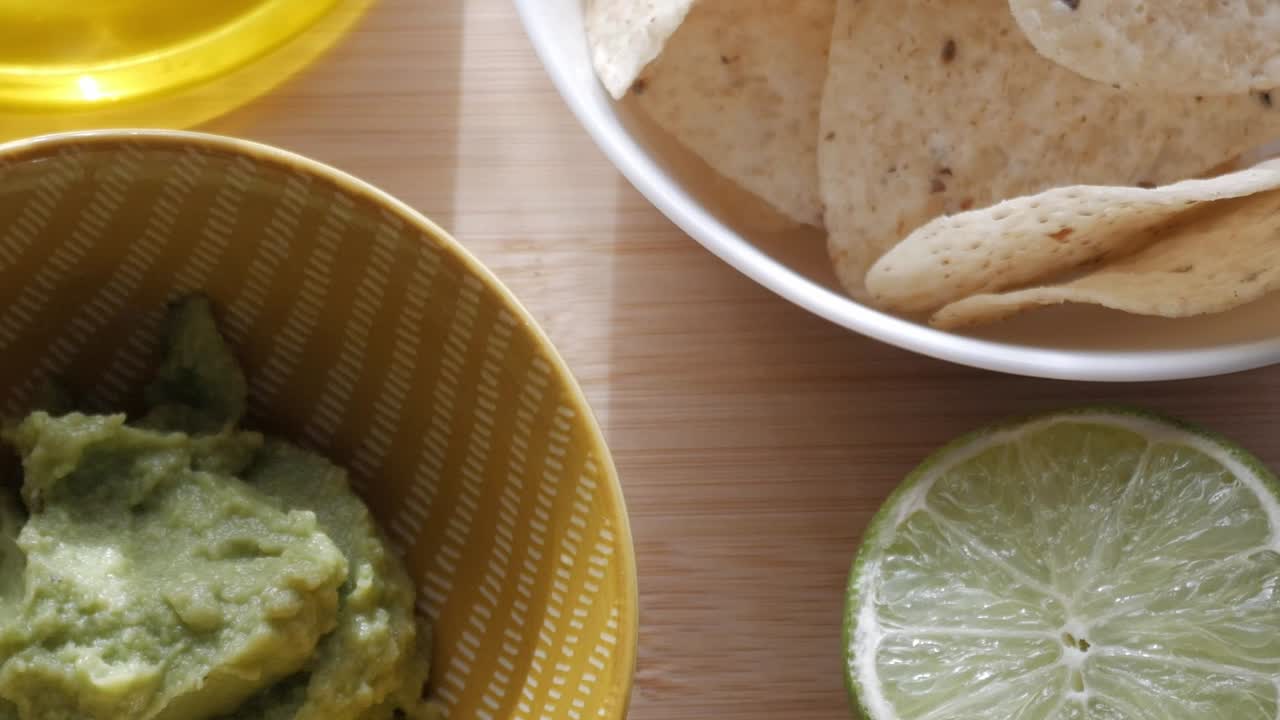 Guacamole in a bowl with tortilla chips and a lime slice on a wooden surface