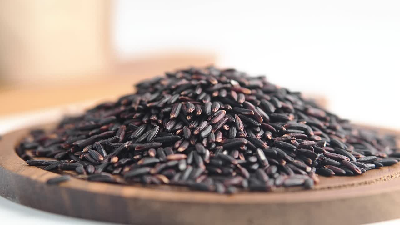 Primo piano di chicchi di riso nero crudi su un piatto di legno.