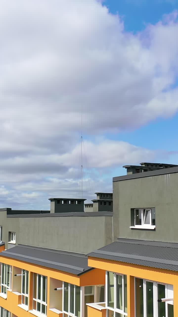 Modern architecture in the city. Tall building with grey roof in the city. New residential apartment building under blue sky. Camera rising. Vertical video