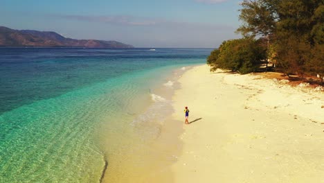 Young-man-fishing-on-clear-sea-water-of-turquoise-shallow-lagoon,-throwing-rod-from-sandy-beach-inside-blue-deep,-Bali