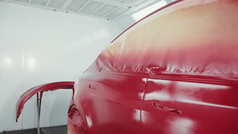 red car undergoing paint job in a spray booth