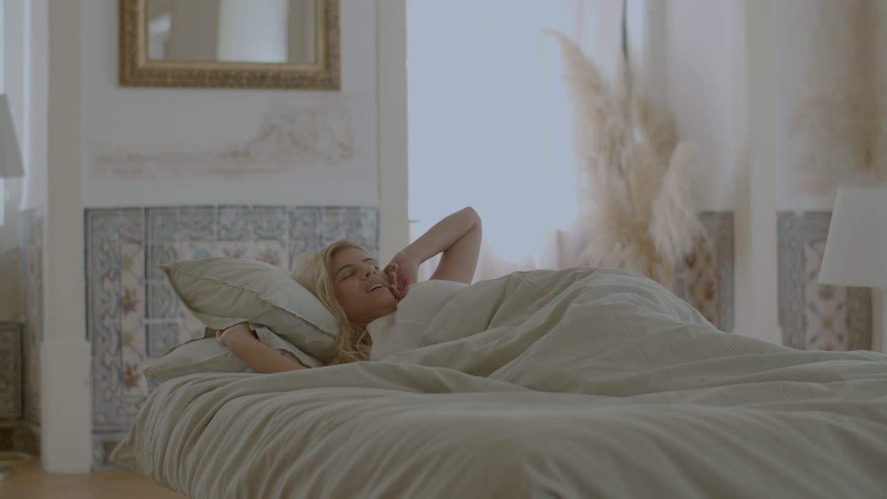 아름다운 여자가 침대에서 깨어나고,  ⁇ 어서  ⁇ 고 있습니다.