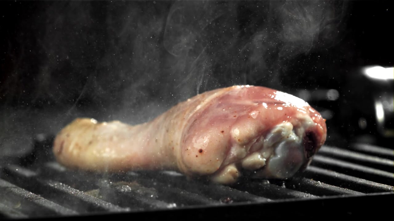 Coscia di pollo cruda sfrigolante su una griglia calda con fumo
