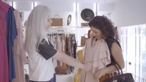 happy female friends choosing clothes with the help of a shop assistant