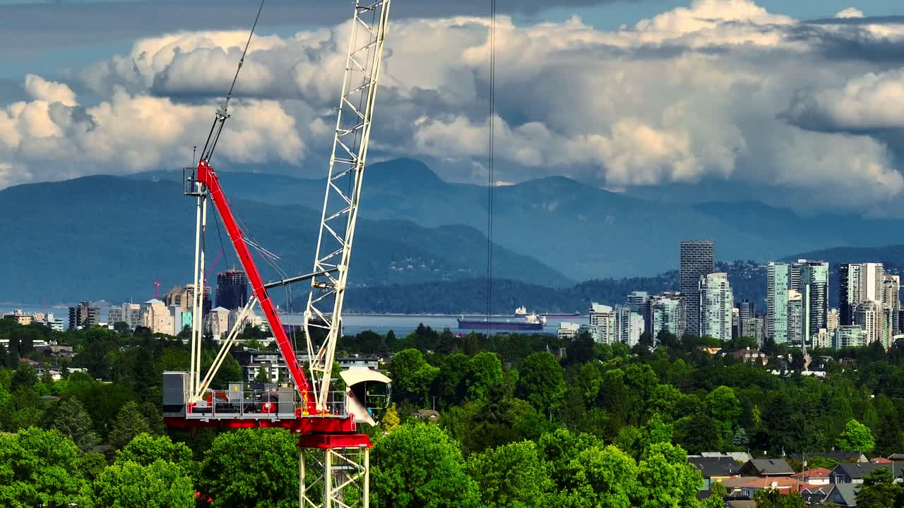 Construction Crane Above Green Trees In Kerrisdale With City Skyline Of Vancouver And Mountains In Background. orbiting drone shot