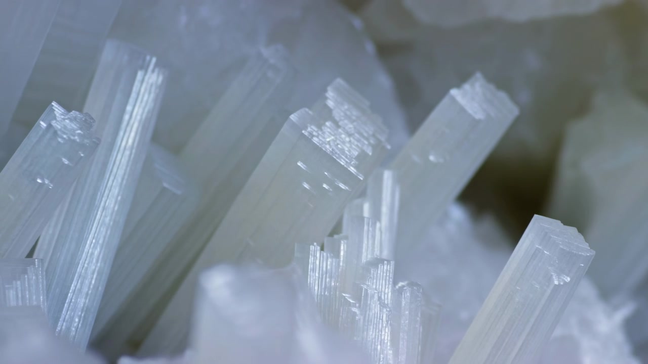 Primo piano di lame minerali traslucide simili a cristalli che riempiono il centro e il lato destro dell'inquadratura, con uno sfondo sfocato e pallido e una luce diffusa fredda