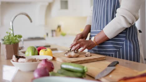 Feliz-Mujer-Mayor-Afroamericana-En-Delantal-Cortando-Verduras-En-La-Cocina,-Cámara-Lenta