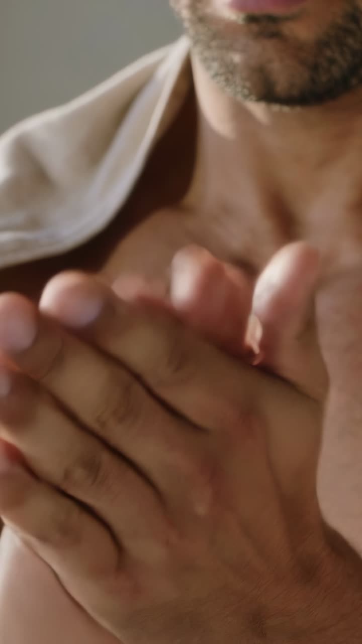 Vertical video: Pressing pump bottle, man dispensing oil into hands at sink, rubbing beard, towel