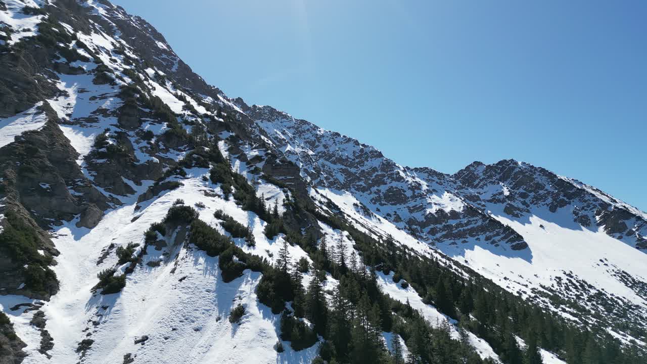 Drone view of Oberjoch in the Bavarian Alps showing snow patches, green meadows, and forested hills. A peaceful mountain village perfect for nature and travel visuals.