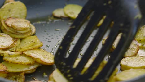 close up of crispy thinly sliced potatoes being cooked outside in frying pan and being gently turned in slow motion with herbs de provence and olive oil 4k