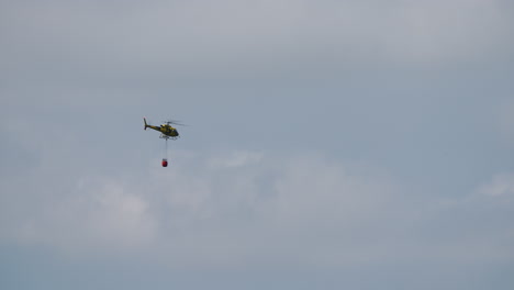 yellow firefighting helicopter carrying a red bambi bucket while flying in the sky