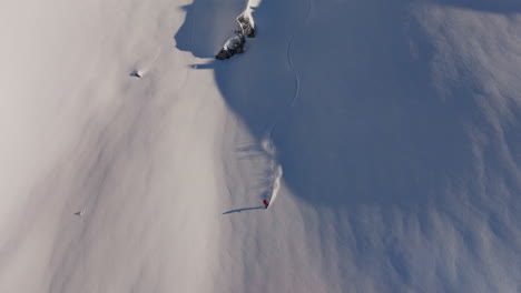 aerial drone shot of a snowboarder carving fresh powder down steep verbier slopes on a pristine bluebird day, white spray and dramatic alpine peaks in the background
