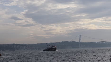 boat cruising near bosphorus bridge which connects europe and asia in istanbul, turkey - wide shot