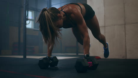 una mujer hace flexiones con pesas. burpee con pesas. la sacudida de las pesas sobre tu cabeza. una mujer entrena con un peso pesado.